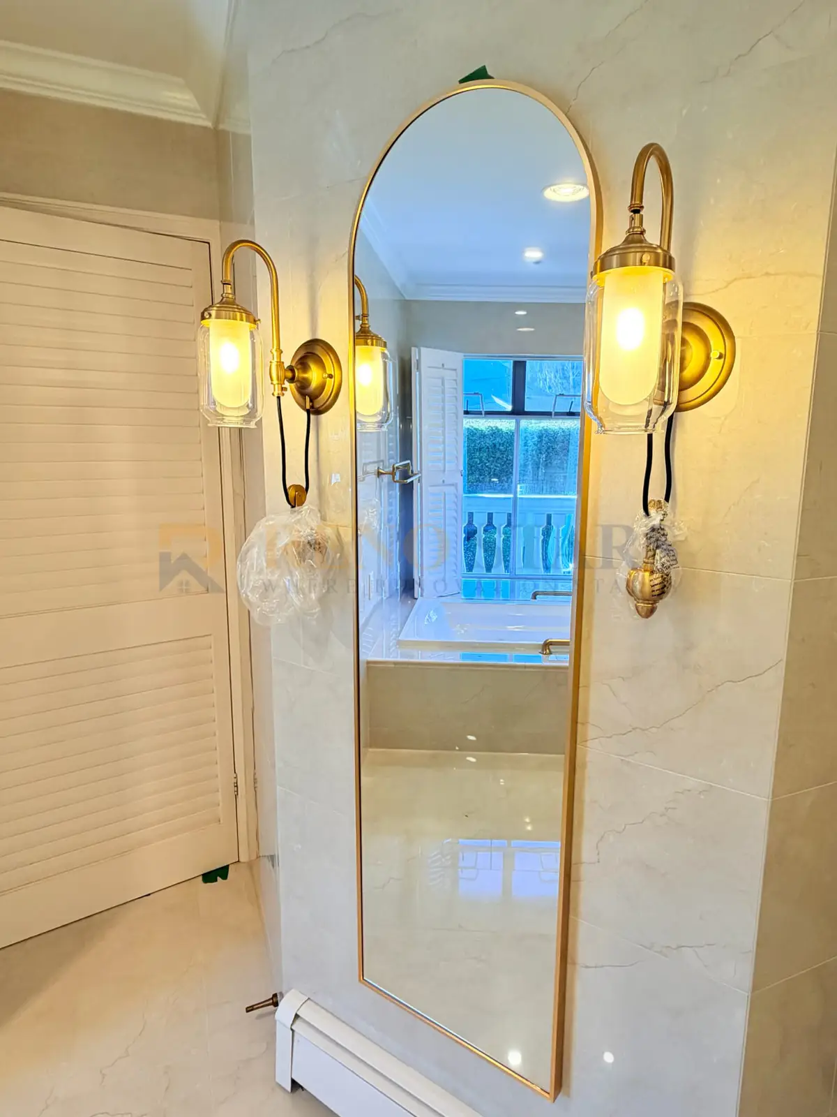 After: champagne gold arched mirror with vintage brass wall sconces and marble wall tiles