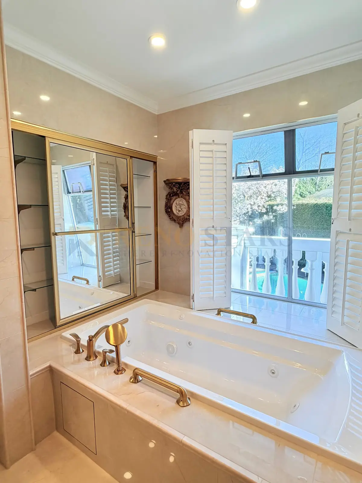 West Vancouver master bathroom after renovation: cream marble tile, champagne gold fixtures, arched mirror