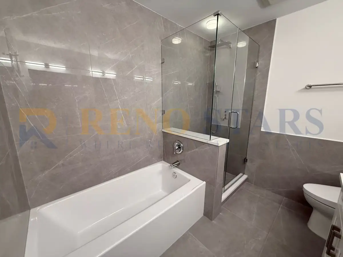 Baño moderno con ducha de vidrio, bañera y elegantes paredes de azulejos grises.